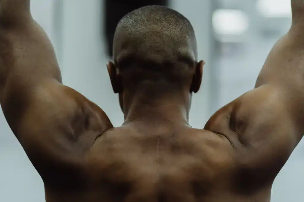 A fit male raising both arms overhead to display sharp posterior delts built with Rear Delt Exercises